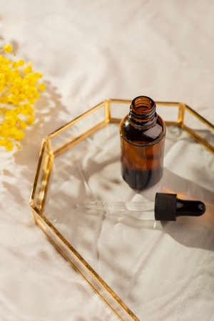Open bottle with dropper pipette with serum or essential oil on glass plate for product...