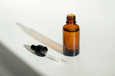 Open bottle with dropper pipette with serum or essential oil. White background with daylight....