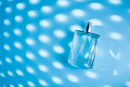 Transparent bottle of perfume on a blue background. Fragrance presentation with daylight. Trending concept with beautiful shadow. Womens essence.の写真素材