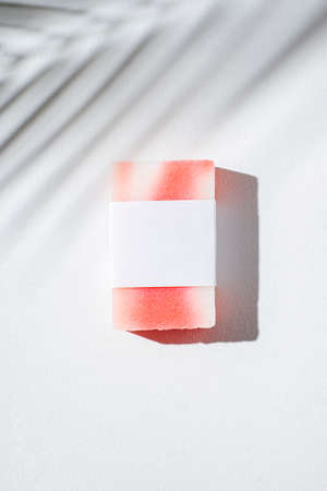Bar of homemade soap with label on a white background. Mockup for design. Skincare cosmetic with shadows from palm leaves. Beauty concept for face body careの写真素材