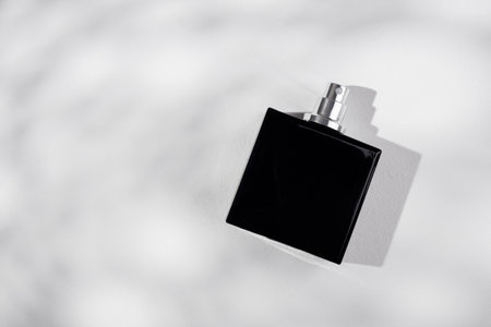 Black bottle of perfume on a white background. Fragrance presentation with daylight. Trending...