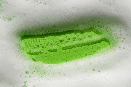 Foam on a green background. Soapy liquid texture with bubbles. Natural sunshine and shadows. Skincare cleansing cosmetic in top view. Frame for textの写真素材