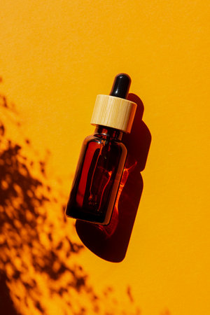 Amber glass bottles with dropper pipette with serum or essential oil on orange background. Skin care cosmetic presentation with daylight and with beautiful plant shadow. Beauty concept for faceの写真素材