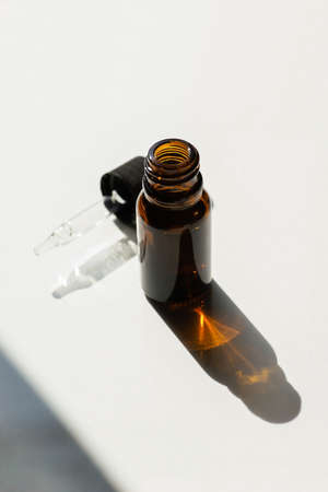 Open bottle with dropper pipette with serum or essential oil. White background with daylight. Skin...