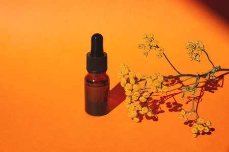 Bottle with dropper pipette with serum or essential oil. Orange background with daylight and yellow flowers. Skincare products, natural cosmetic. Beauty concept for face and body careの写真素材