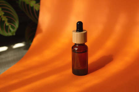 Bottle with dropper pipette with serum or essential oil. Orange background with daylight and beautiful shadows. Skincare products , natural cosmetic. Beauty concept for face and body careの写真素材