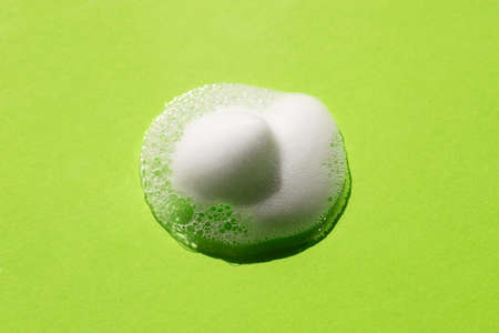 Foam on a green background. Soapy liquid texture with bubbles. Natural sunshine and shadows. Skin care cleansing cosmetic in top view.の写真素材
