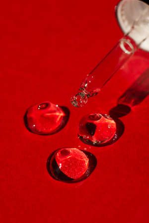Open cap with close-up dropper pipette with serum. Red background with daylight and the appearance of the texture of the gel. Skin care products, natural cosmetic.の写真素材