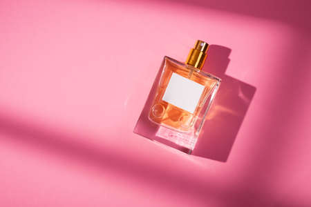 Transparent bottle of perfume with label on a pink background. Fragrance presentation with daylight. Trending concept in natural materials with beautiful shadow. Womens and mens essence.の写真素材