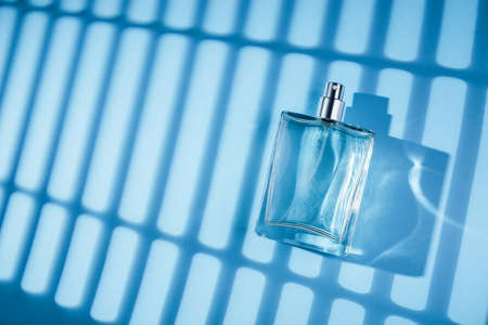 Transparent bottle of perfume on a blue background. Fragrance presentation with daylight. Trending...