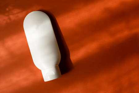 Plastic white tube for cream or lotion. Skin care or sunscreen cosmetic in top view on orange...