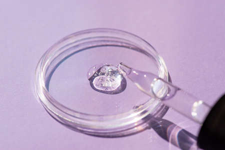 Dropper pipette with serum or cosmetic liquid i on purple in a transparent container on purple background. Transparent container with liquid and bubbles. The appearance of the texture of the gel.の写真素材