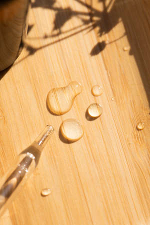 Pipette close-up with drops on the wooden surface in soft focus. Beautiful shadow in the sunlight. Skincare products, natural cosmetic. Beauty concept for face and body careの写真素材