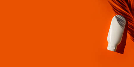 Plastic white tube for cream or lotion on an orange background. Top view with palm leaves shadow. Skincare sunscreen cosmetic. Beauty concept for face body careの写真素材