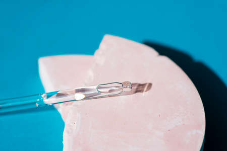 Pipette with serum or cosmetic liquid close-up in soft focus on pink concrete plate for product presentation on blue background. Skincare products, natural cosmetic. Beauty concept for faceの写真素材