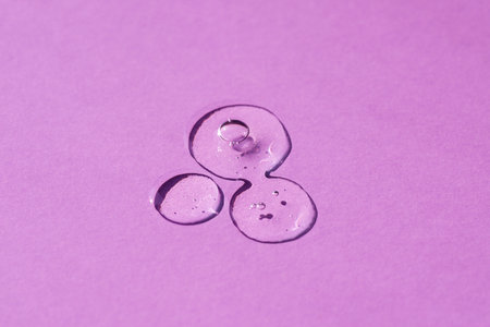Transparent drop of cosmetic product serum gel. Liquid texture with bubbles on purple background in top view. Skincare products, natural cosmetic. Beauty concept for face and body careの写真素材