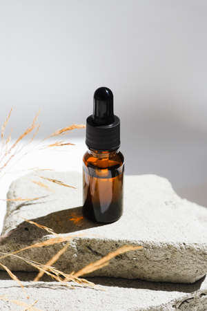 Amber glass dropper with black lid and dry plant. Bottle on grey concrete podium for product presentation. Skincare cosmetic. Beauty conceptの写真素材