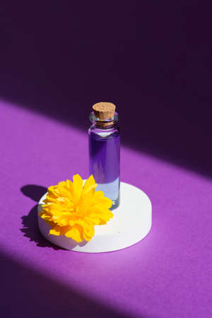 Lavender or lilac essential herb oil in a glass bottle on a podium with yellow flower on purple background. Skincare products, natural cosmetic. Beauty concept for face and body careの写真素材