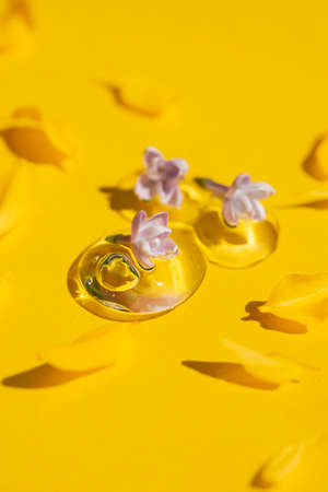 Transparent drops of cosmetic product serum or gel with lilac flowers and yellow petals. Liquid texture with bubbles. Cosmetic smear. Beauty concept for face and body careの写真素材