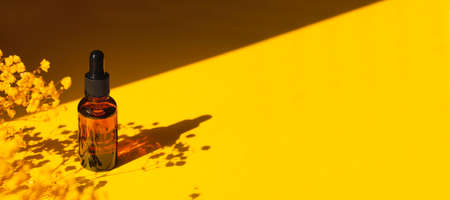 Amber bottle with dropper pipette with serum or essential oil. Yellow background with daylight with...