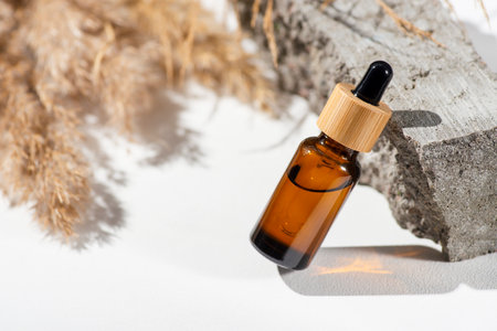 Amber glass dropper with bamboo lid and dry plant. Bottle on grey concrete podium for product presentation. Skincare cosmetic with wildflowers. Beauty conceptの写真素材