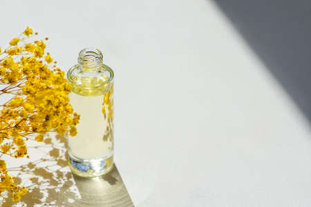 Open transparent bottle without cap with serum or essential oil with beautiful yellow flowers. White...