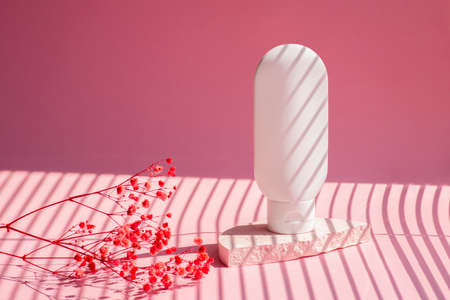 Plastic white tube for cream or lotion on pink background. Skin care cosmetic with beautiful shadows with red flowers. Beauty concept for face body care.の写真素材