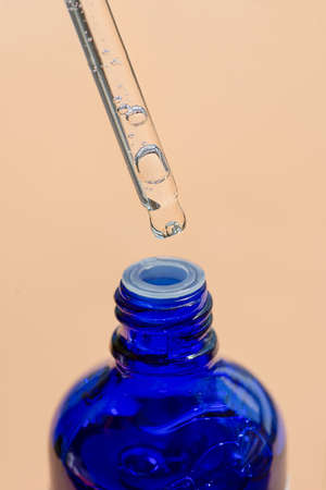 Dropper pipette with serum or oil with blue bottle. Skincare products, natural cosmetic on beige...