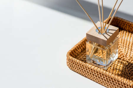 Transparent bottle of aroma diffuser in a wicker basket on white background. Eau de parfume for home...