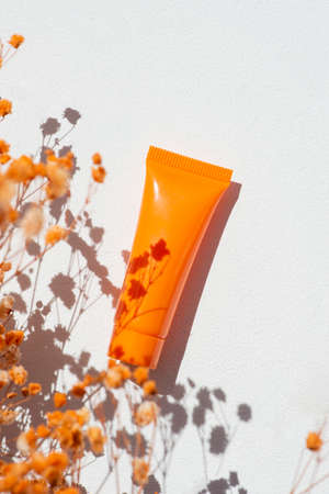 Plastic orange bottle for cream or lotion on a white background. Skincare cosmetic with orange flowers. Beauty concept for face body careの写真素材