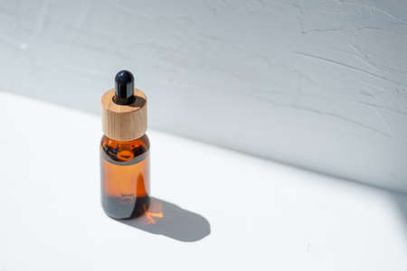 Bottle with dropper pipette and serum or essential oil. White background with daylight and beautiful...