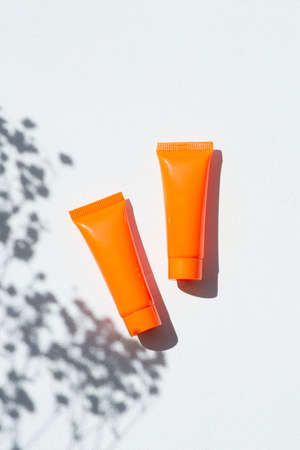 Plastic orange bottle for cream or lotion on a white background. Skincare cosmetic with flowers shadows. Beauty concept for face body careの写真素材
