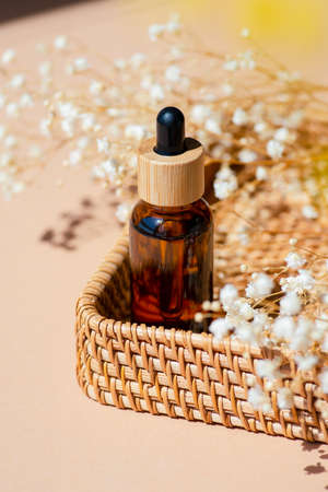 Amber bottle with dropper pipette in a wicker basket. Beige background with daylight and beautiful shadows. Skincare serum or essential oil natural cosmetic. Beauty concept for face and body careの写真素材