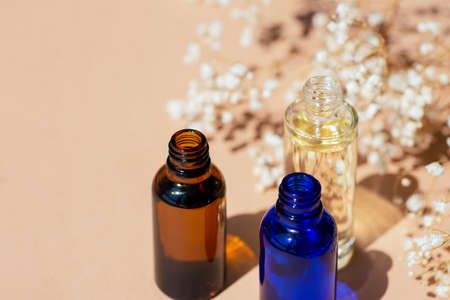 Open amber, blue and transparent bottles without cap with serum or essential oil with white flowers....