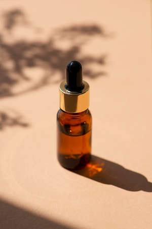 Bottle with dropper pipette with serum or essential oil. Beige background with daylight and beautiful shadows. Skincare products, natural cosmetic. Beauty concept for face and body careの写真素材