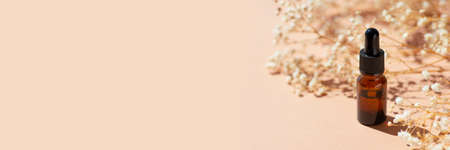 Amber bottle with dropper pipette with serum or essential oil. Beige background with daylight with beautiful flowers and shadows. Skincare natural cosmetic. Beauty concept for face and body careの写真素材