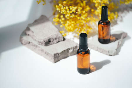 Amber pump bottles with serum, tonic or essential oil on grey concrete podium with yellow flowers. White background with daylight. Beauty concept for face and body careの写真素材