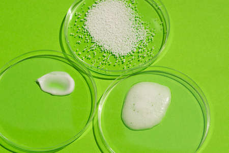 Cosmetic swatches. Appearance of the texture of the cream, mask, foam and granules in petri dish on a green background. Natural skincare products. Beauty concept for face and body careの写真素材
