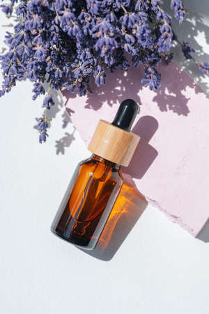 Amber dropper bottle with serum, tonic or essential oil on pink concrete podium. White background...