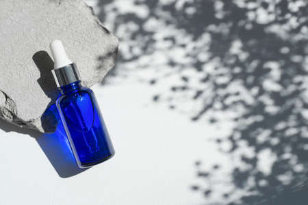 Blue dropper bottles with serum, tonic or essential oil on grey concrete podium. White background with daylight with flowers shadows. Beauty concept for face and body careの写真素材