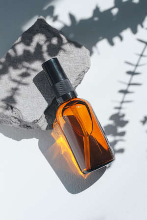 Amber pump bottle with serum, tonic or essential oil on grey concrete podium with eucalyptus shadows. White background with daylight. Beauty concept for face and body careの写真素材
