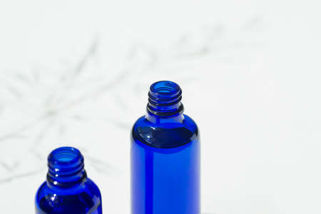 Open blue bottle with serum or essential oil. White background with daylight and beautiful shadows....