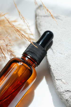 Amber glass dropper with black lid and dry plant. Bottle on grey concrete podium for product presentation. Skincare cosmetic with wildflowers. Beauty conceptの写真素材