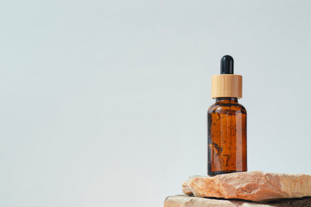 Amber dropper bottle with serum or gel on stone podium. White background. Beauty concept for face and body care. Skincare products, natural cosmetic.の写真素材