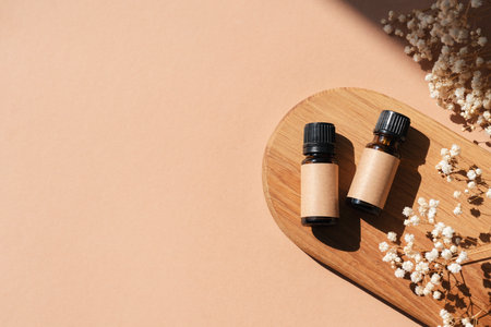 Amber bottles with craft label filled serum, tonic or essential oil on wooden tray and dry flowers. Beige background with daylight . Beauty concept for face and body care. Copy spaceの写真素材