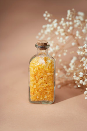 Transparent bottle filled with yellow bath sea salt on beige background. Beauty treatment for spa...