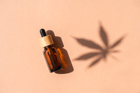 Amber glass dropper bottles with cannabis oil used for medical purposes on beige background. Daylight and the shadow of a hemp leaf. Soothing cbd oil. Alternative Medicine. Copy spaceの写真素材