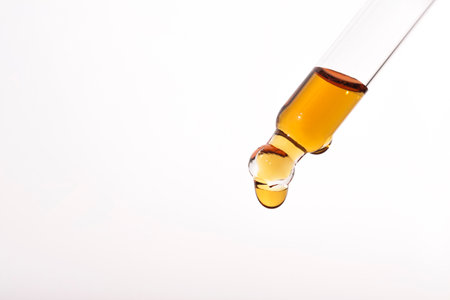 Pipette with drop of serum or cosmetic liquid close-up on white background. The appearance of the texture of the gel. Transparent laboratory glassware. Medicine and beauty concept.の写真素材