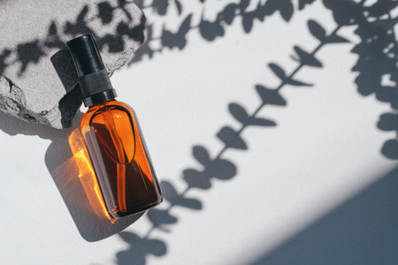 Amber pump bottle with serum, tonic or essential oil on grey concrete podium with eucalyptus shadows. White background with daylight. Beauty concept for face and body careの写真素材