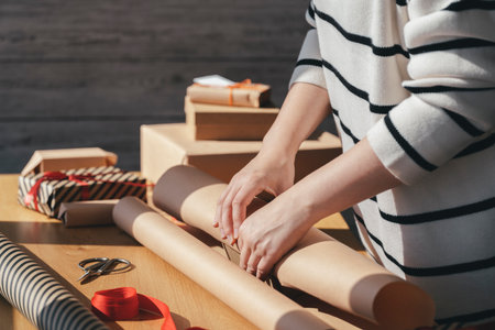 Young woman packing a box in craft paper on a wooden table. Preparation of gifts for the celebration. Giftbox wrapping in eco packaging.の写真素材